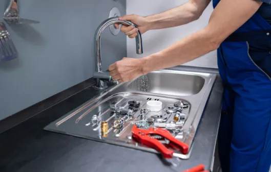 Plumber testing a kitchen sink faucet with tools and spare parts placed on the counter nearby.