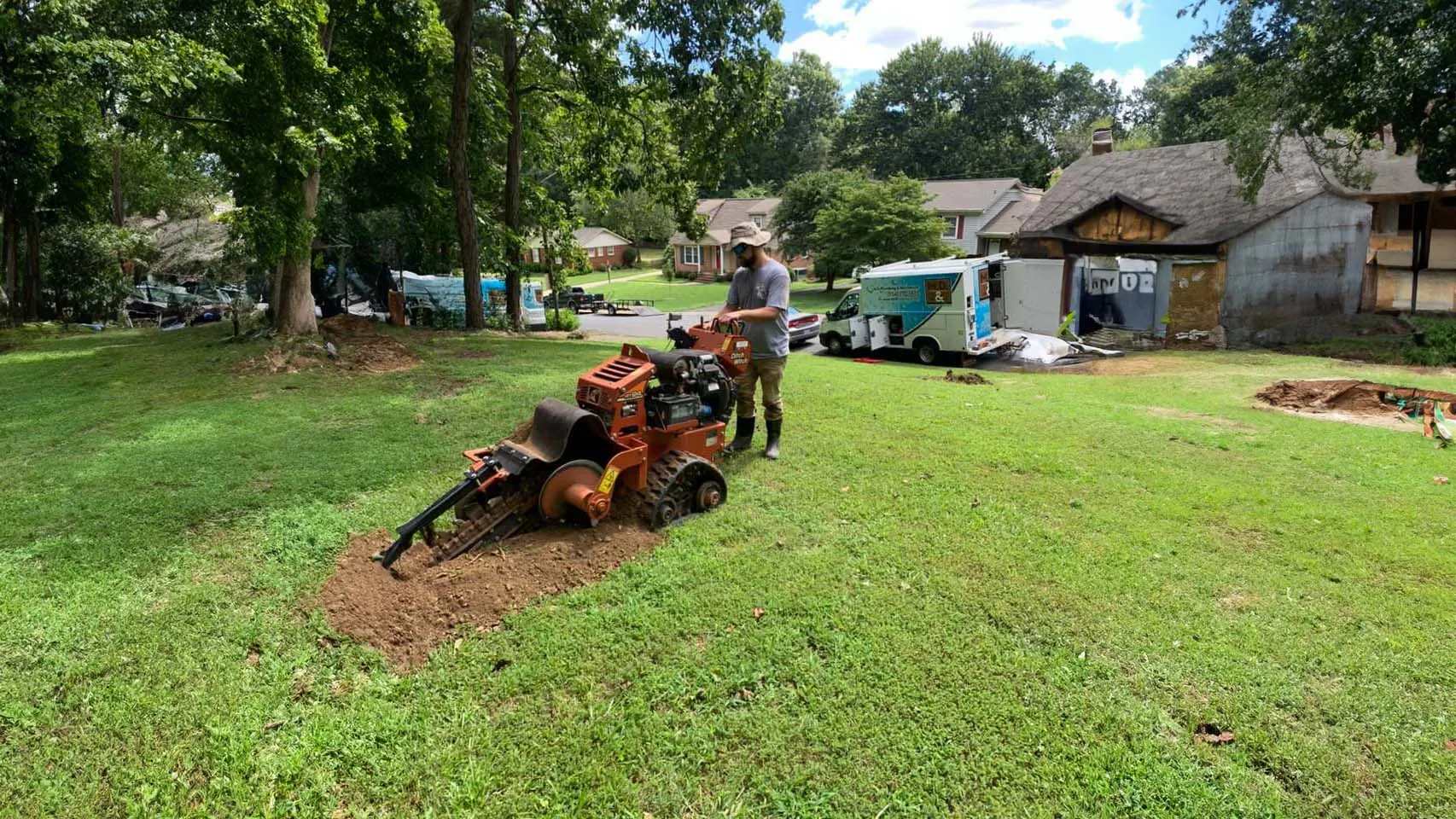 Worker operating a trenching machine on a residential lawn for underground plumbing installation.