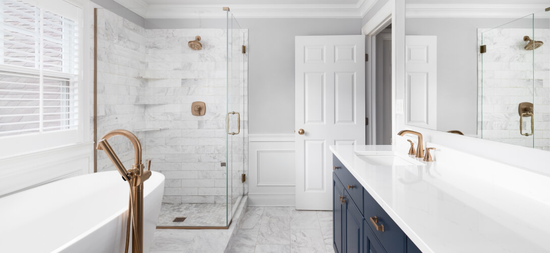 Luxurious bathroom with a modern white marble shower, freestanding bathtub, navy blue vanity, and gold fixtures.