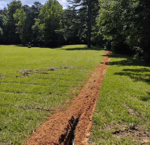 Freshly dug trench in a grassy yard for underground plumbing or utility line installation.