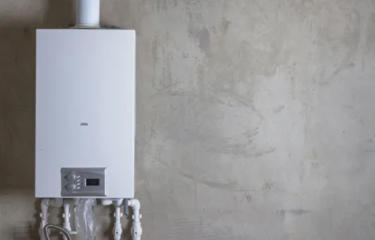 Wall-mounted tankless water heater with connected pipes in a minimalistic indoor setting.